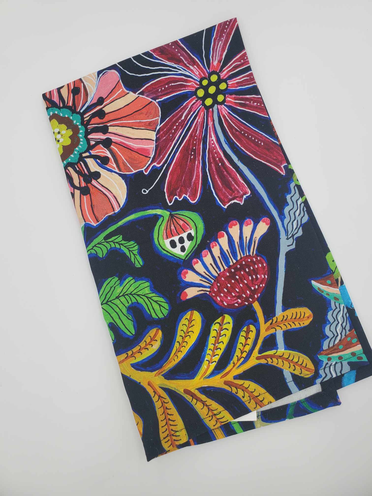 Folded Lori Siebert tea towel with vibrant colors on a black  back drop. 